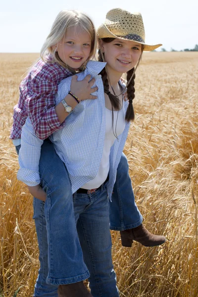 Young midwestern cowgirls play piggyback — Stock Photo, Image