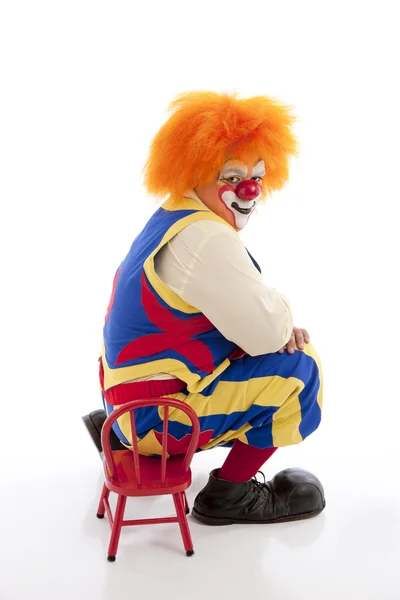 Un clown professionista si siede su una sedia minuscola — Foto Stock