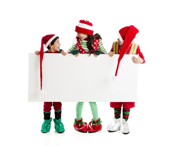 Drei der Weihnachtselfen halten ein leeres Schild für Ihre Urlaubswerbung bereit. — Stockfoto