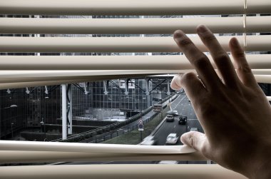 Man at office opening window blinds and seeing city streets and clipart