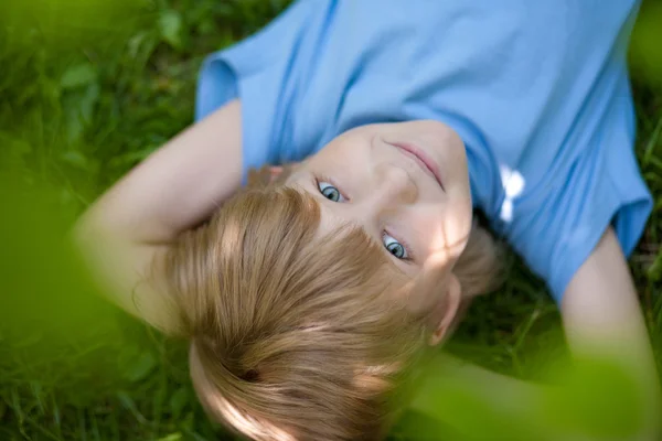 Kleine jongen in bkue t-shirt liggen op het gras — Stockfoto