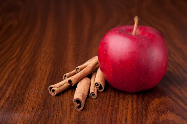 Roter Apfel auf dunklem Holztisch mit Zimtstangen — Stockfoto