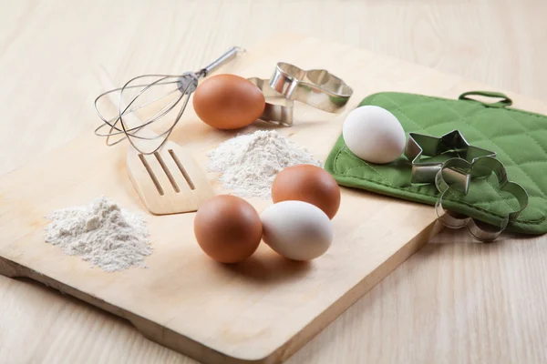 Uova, farina, stampo per biscotti e frusta su tavola di legno — Foto Stock