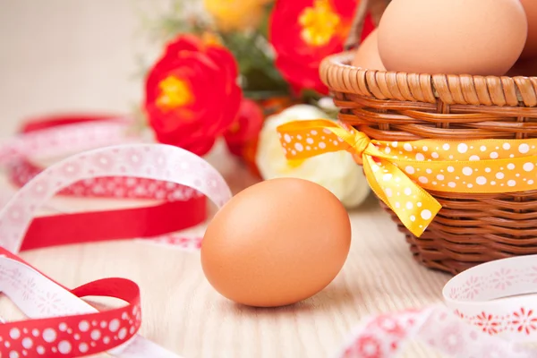 Un huevo cerca de una pequeña cesta con cintas y flores en madera ta — Foto de Stock