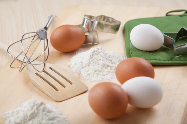 Uova, farina, stampo per biscotti e frusta su tavola di legno — Foto Stock