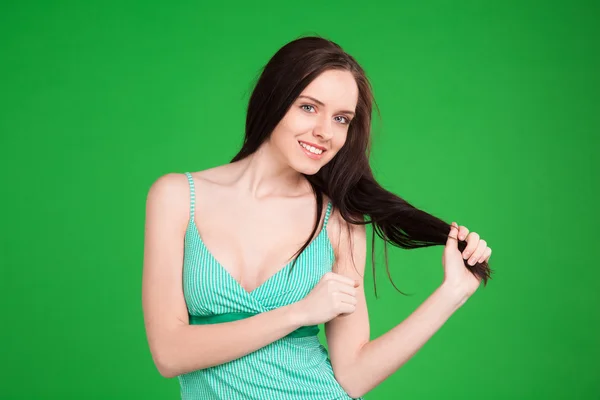 Улыбающаяся брюнетка, держа волосы на зеленом фоне — стоковое фото
