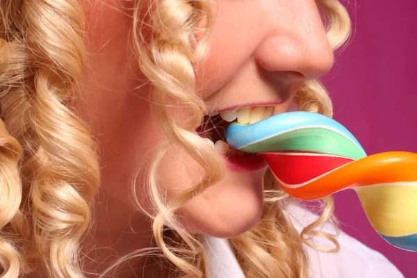 Woman with blonde curly hair biting bright lollipop over pink background — Stock Photo, Image