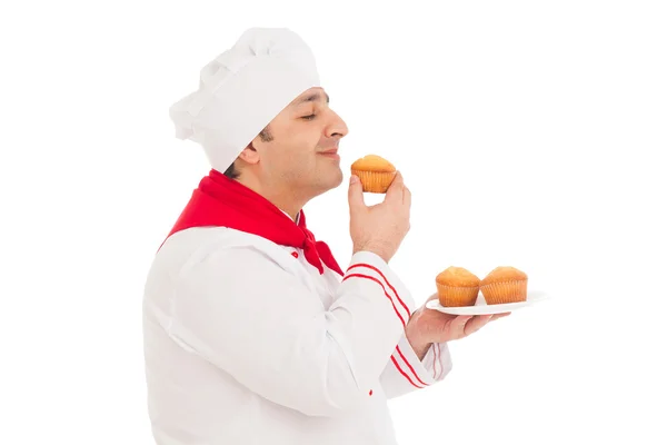 Lächelnder Koch, der leckeren Muffin in roter Uniform riecht — Stockfoto