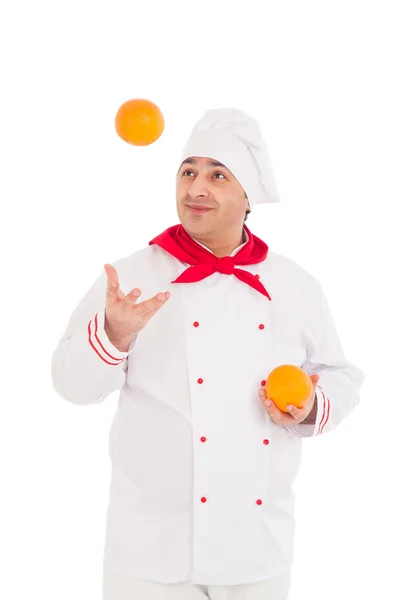 Feliz chef sosteniendo dos naranjas vistiendo uniforme rojo y blanco — Foto de Stock
