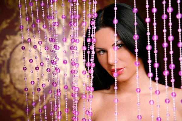 Sexy brunette woman loking through pink beads — Stock Photo, Image