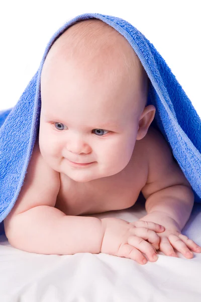 Een mooie glimlachende baby onder een blauwe handdoek — Stockfoto