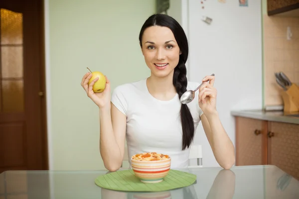 Chica morena desayunando con muesli y manzana en casa en —  Fotos de Stock
