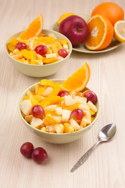 Two bowls with fruit salad on wooden table with spoon — Stock Photo, Image