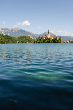 Bled Gölü 'nün manzarası. Maria' nın Varsayımı Kilisesi 'nin bir adada olması ve Slovenya' nın dağları ve ormanı olan Bled Kalesi.