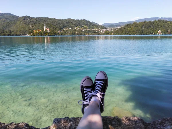 黒と白の靴をはっきりとターコイズブルーに座っている旅行者マリア教会を望む湖 スロベニア — ストック写真