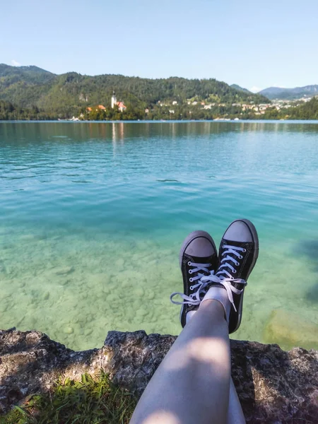黒と白の靴をはっきりとターコイズブルーに座っている旅行者マリア教会を望む湖 スロベニア — ストック写真