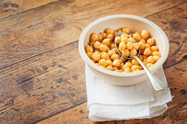 Cooked chickpeas in white bowl on wooden background. Spilled chickpeas. Vegetarian food concept. Macrobiotic diet.