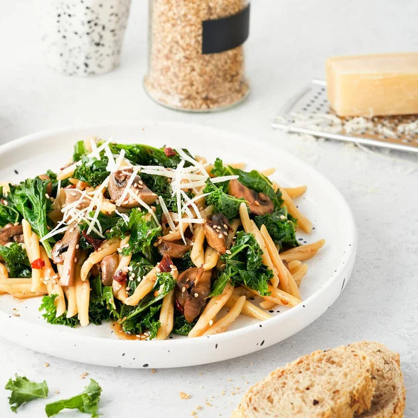 Whole grain pasta with kale, mushrooms, parmezan cheese in white plate on light background. Vegetarian Healthy diet concept. Recipe step by step.