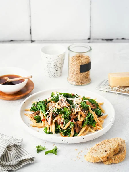Whole grain pasta with kale, mushrooms, parmezan cheese in white plate on light background. Vegetarian Healthy diet concept. Recipe step by step. Copy space for text.
