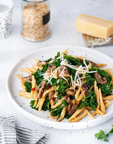 Whole grain pasta with kale, mushrooms, parmezan cheese in white plate on light background. Vegetarian Healthy diet concept. Recipe step by step.