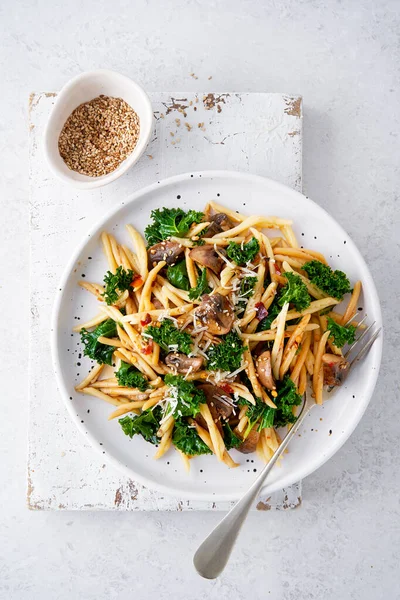Whole grain pasta with kale, mushrooms, parmezan cheese in white plate on light background. Vegetarian Healthy diet concept. Recipe step by step. Copy space for text. Top view.