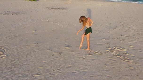 若い美しい少女バレリーナは黄金の夕日の海の近くのビーチで踊っています 女性はビーチで踊っているドローンは円の中で彼女の周りを飛ぶ — ストック動画