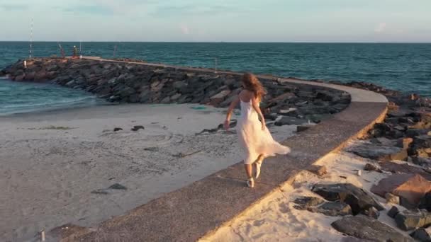 若い美しい少女バレリーナは黄金の夕日の海の近くのビーチで踊っています 感動的な女性 魅力的な女優の笑顔 バレリーナは海のそばで踊り無人機は彼女を追う — ストック動画