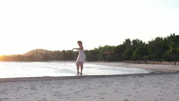 若い美しい少女バレリーナは黄金の夕日の海の近くのビーチで踊っています 感動的な女性 魅力的な女優の笑顔 海岸のダンサーの近くでドローンが飛ぶ — ストック動画