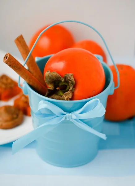 Beautiful blue bucket with persimmon and cinnamon. — Stock Photo, Image