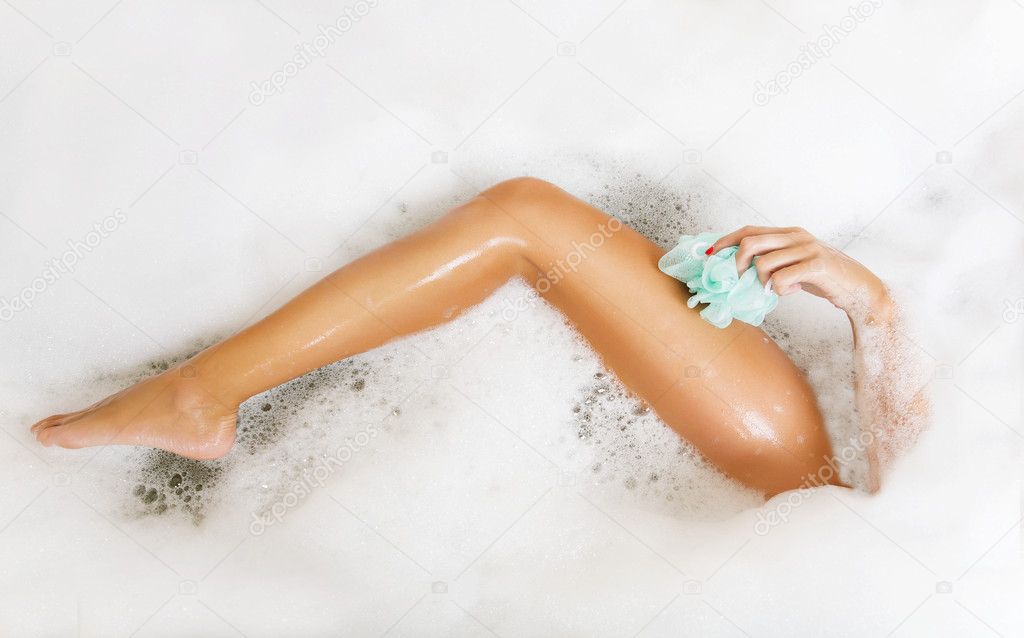 Woman in bath washing leg in bathtub with a lot of bubble bath foam.