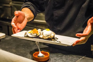 Şef bir çift çiğ Galiçya istiridyesi hazırlıyor ve tabakta servis yapıyor.