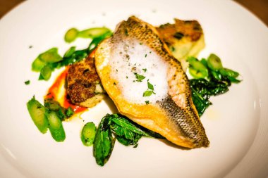 Izgara deniz kabuğu balığı, beyaz tabakta cin, köpük ve sebze.