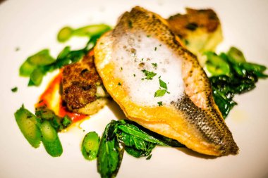 Izgara deniz kabuğu balığı, beyaz tabakta cin, köpük ve sebze.