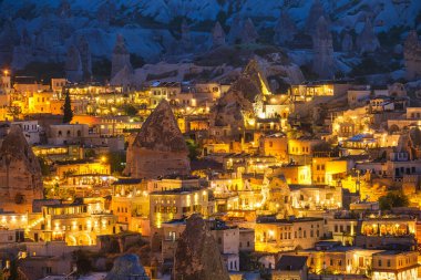 Goreme, Kapadokya, Türkiye. Dağdan akşam şehri manzarası. Parlak akşam şehri. Yaz mevsiminde manzara. UNESCO mirası. Tatil ve turizm.