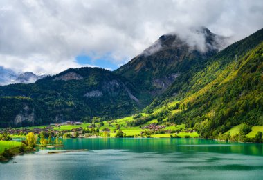Lungern, Obwalden, İsviçre kantonu. Yeşil bir çayırdaki kırsal evlerin manzarası. Dağ vadisinde bir göl. Seyahat etmek için popüler bir yer.