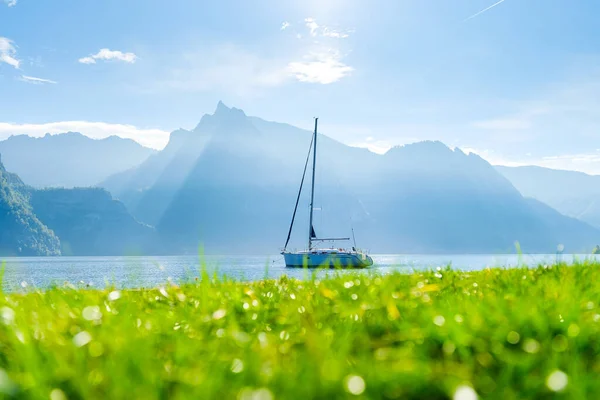 A yacht against the backdrop of the mountains in Switzerland. Calm water and bright sunny day. A popular place to travel and relax.