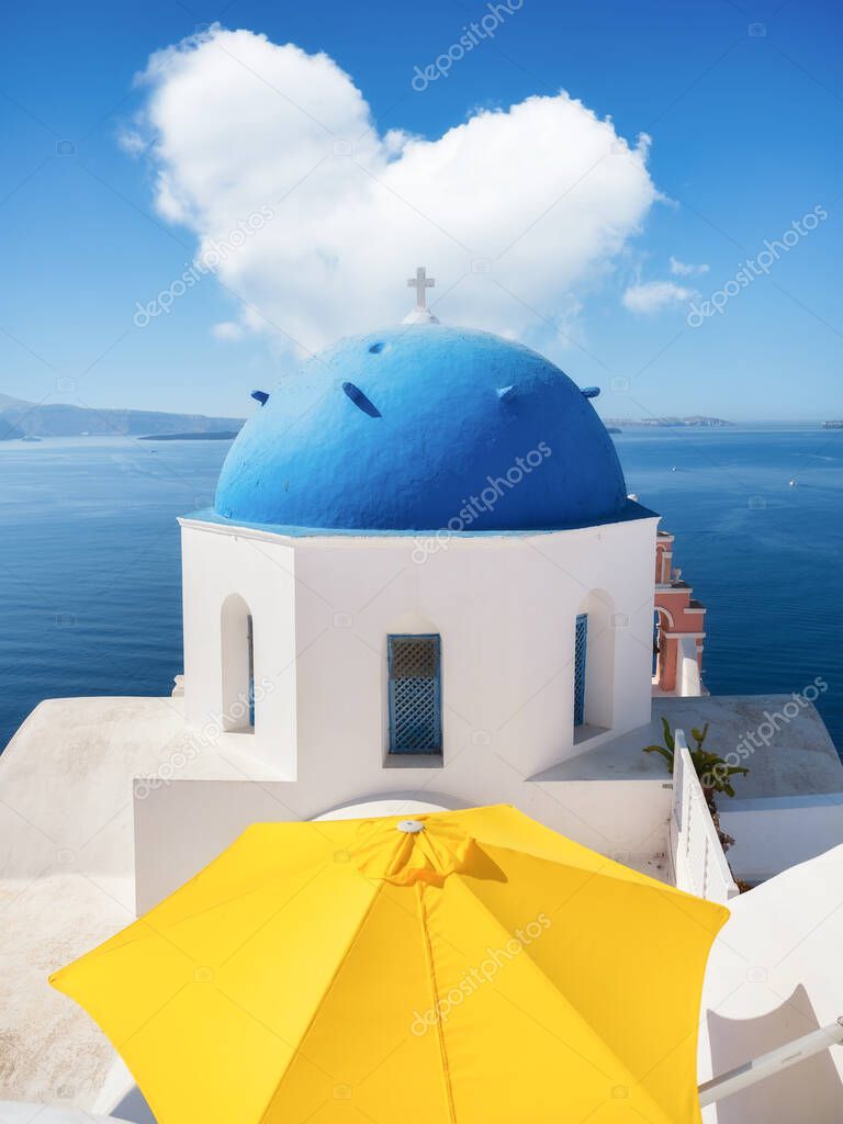 Oia village, Santorini Island, Greece. A cloud in the shape of a heart. A blue sky and a heart sign. View of traditional houses and church in Santorini. Travel and vacation photography.