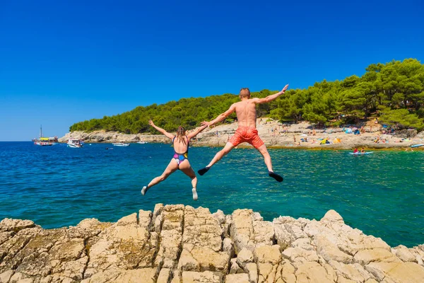 A carefree couple jumps into the azure sea. A vacation in the summertime. Young and energetic people dive into the water together. A fun vacation at the sea together.