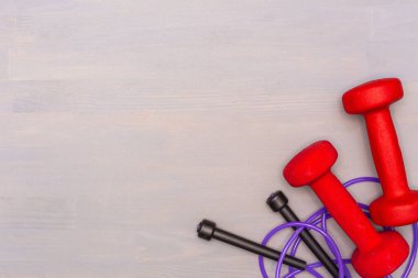 Red dumbbells and purple skipping rope on a wooden gray background