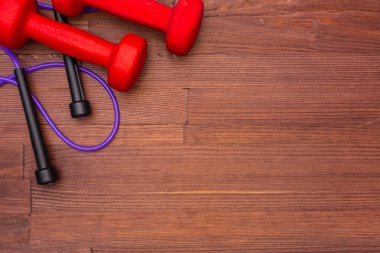 Red dumbbells and purple skipping rope on a wooden brown background