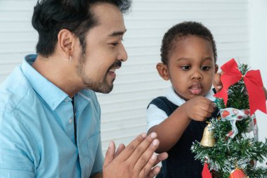Daddy and son enjoy using times to decrorate christmas tree and take a selfie with mobile at home.