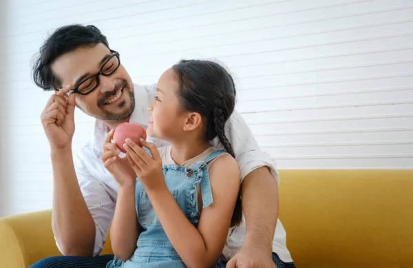 Asian happy family. Father looking his daughter eating apple and very happy.