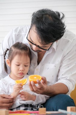 Father teaches daughter to eat oranges and is glad that daughter eats oranges