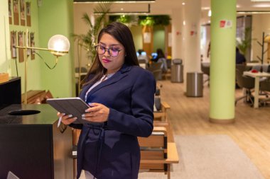 Yoğun, modern bir işyerinde çalışan, telefon tutan veya tablet kullanan genç beyaz bir kadının portresi.