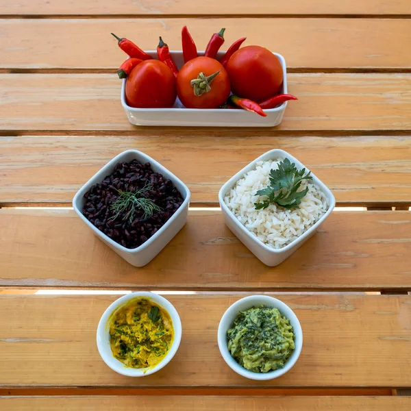 Tabaklar dolusu siyah beyaz pirinç, baharatlı soslar, domatesler ve ahşap masada acı biber. 