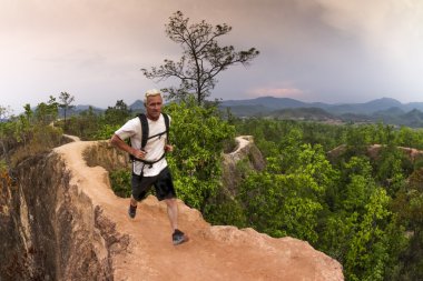 Man hiking and running in mountains wearing white shirt and backpack clipart