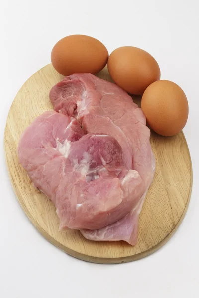 Сырая свинина и яйца на деревянной доске для резки на белой спинке — стоковое фото