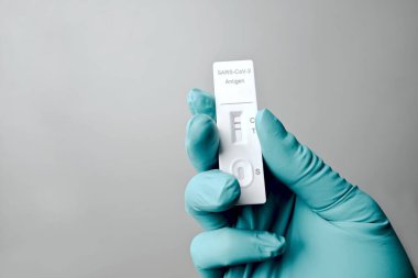 Eldivenli el COVID-19 için pozitif hızlı test cihazı tutuyor. Gri arkaplanda izole.