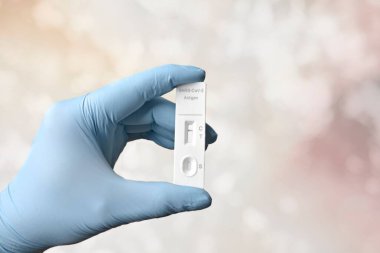 Bokeh arkaplanı önünde COVID-19 için negatif hızlı bir test cihazı tutan eldivenli el.