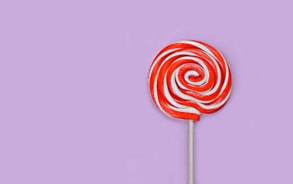 Round white and red lollipop with wooden stick on lilac background.
